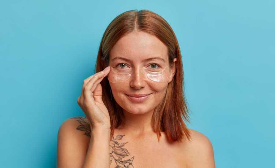 beautiful-redhead-woman-with-clean-fresh-smooth-skin-applies-hydrogel-transparent-patches-eye-skin-care-mask-enjoys-collagent-treatment-stands-shirtless-isolated-blue-wall (2)